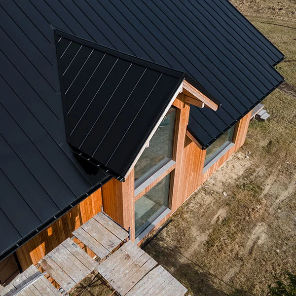 Maison avec un toit en métal noir et un revêtement en bois, équipée d'un protège-gouttière.