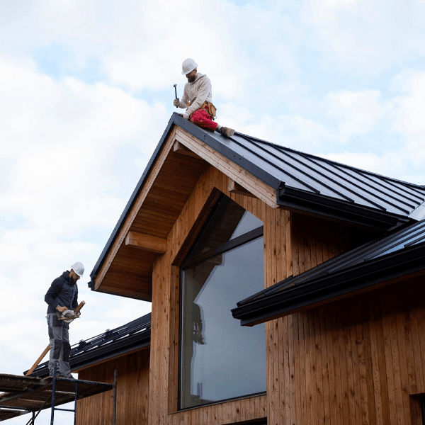 A homeowner using a garden hose to clean and maintain the rain gutters of a house.