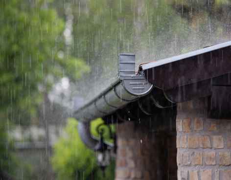 Rainwater flowing into a gutter being covered by a metal grate during a storm.