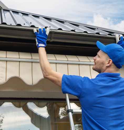 A man in blue shirt and gloves repairing a metal roof.