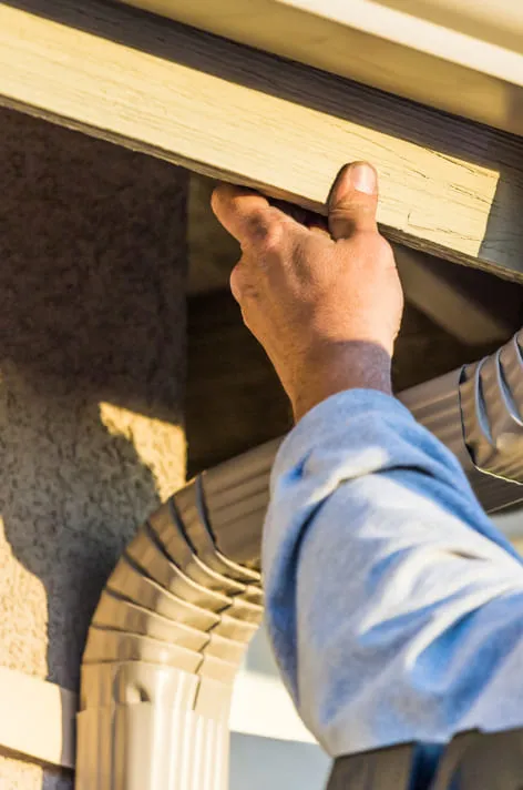 A person performing gutter cleaning by fixing a gutter on a house