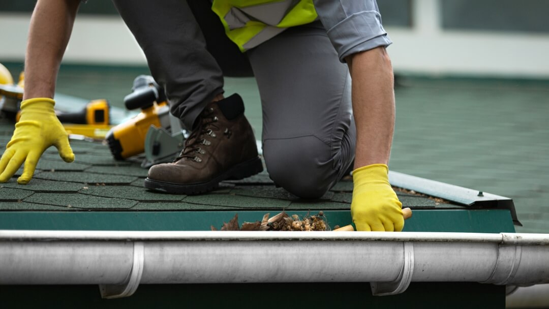 Professional worker in safety gear cleaning debris from a residential rain gutter.